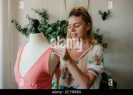 Giovane donna stilista di misura manichino, nastro di fissaggio Seamstress lavorare con manichino in casa accogliente o negozio di sarto, dressmaking e conce cucito Foto Stock