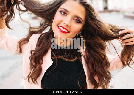 Bella bruna ragazza con luminosi compongono tenendo i suoi capelli e sorridente alla fotocamera. Foto Stock