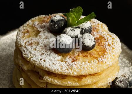 Pancake con mirtilli e zucchero a velo su una vecchia padella di alluminio su sfondo scuro Foto Stock