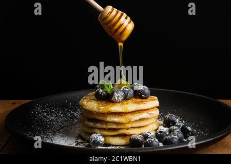 Immergendo il miele sui pancake con mirtilli e zucchero a velo Foto Stock