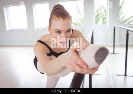 Ballerina caucasica femminile che si concentra sul suo esercizio in uno studio luminoso Foto Stock