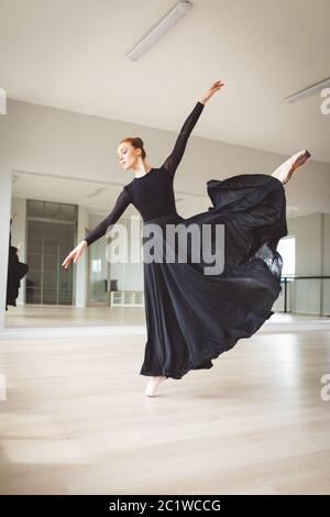 Ballerina caucasica femminile con un abito nero e focalizzata sul suo esercizio in uno studio luminoso Foto Stock