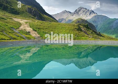 Riflessione di montagna nelle acque turchesi calme di un bacino artificiale in cima alle montagne tirolesi, Austria. Foto Stock