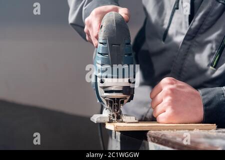 Primo piano di attrezzi per la lavorazione del legno con le mani del falegname. Seghetto alternativo di potenza Foto Stock