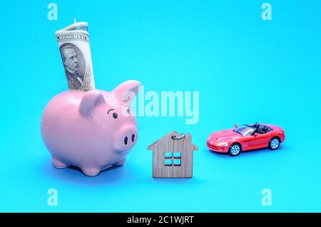 Piggy rosa banca con una casa e una macchina sul tavolo. Oscurata. Concetto di risparmio di finanze e di depositi immobiliari. Foto Stock