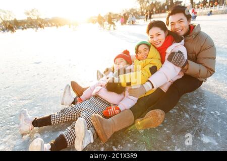 La famiglia felice di quattro sedette giocando sul ghiaccio Foto Stock