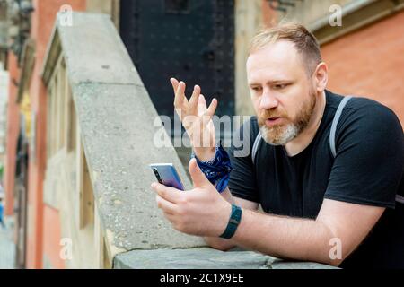 un uomo adulto parla con uno smartphone in un centro città. l'uomo ha una videochiamata con uno smartphone Foto Stock