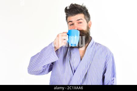 Uomo con barba e baffi mantiene la tazza di caffè isolato su bianco. Caffè del mattino concetto. Macho in accappatoio bevande di tè o caffè con la faccia del sonno. Guy guarda assonnato, necessita di caffè. Foto Stock