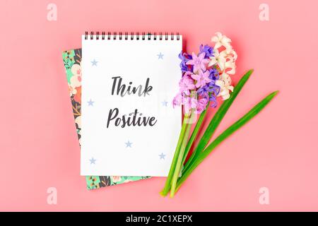 Taccuino bianco per note, bouquet di fiori giacinti su sfondo rosa piatto Lay Top view testo Think Positive - motational slogan concetto creativo Foto Stock