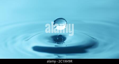 una goccia d'acqua gocciola nell'acqua blu, formando increspature, primo piano Foto Stock