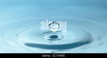 una goccia d'acqua gocciola nell'acqua blu, formando increspature, primo piano Foto Stock