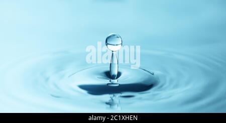 una goccia d'acqua gocciola nell'acqua blu, formando increspature, primo piano Foto Stock