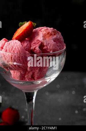 palle di gelato alla fragola con fragole, in un vetro ad alta trasparenza su sfondo scuro Foto Stock