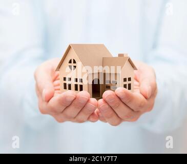 Di proprietà di assicurazione. Casa di cartone miniatura in mani Foto Stock