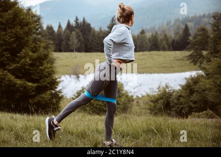 Primo piano giovane donna sportiva fare esercizio con la banda terapeutica al parco in estate, esercizio resistivo Foto Stock