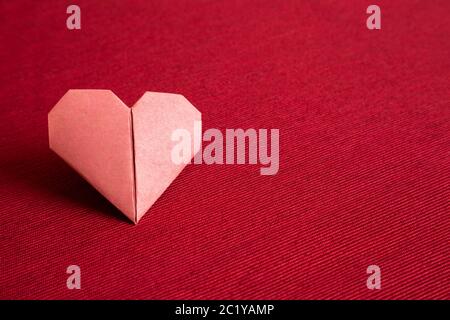 Carta rossa cuore origami su fondo tessuto rosso. Copia spazio Foto Stock