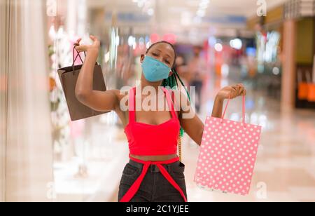 Giovane donna afroamericana al centro commerciale in nuova normalità dopo covid-19 - ragazza nera felice e bella in maschera di faccia che tiene i sacchetti di shopping enjoyin Foto Stock