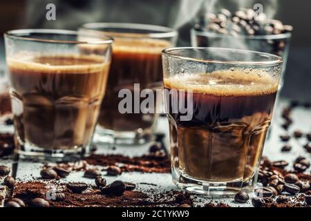 Caffè in tazze di vetro mescolate con crema e chicchi di caffè spruzzati Foto Stock