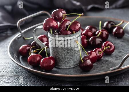 Vassoio vintage metallizzato, superficie e tazza con ciliegie rosse succose all'interno della tazza e sparse intorno al vassoio Foto Stock