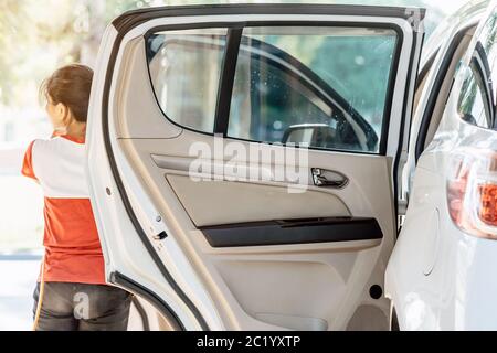 Donna che pulisce con un soffiatore e pulisce la microfibra l'auto che pulisce dopo il lavaggio dell'automobile. Messa a fuoco selettiva su una porta dell'automobile. Foto Stock