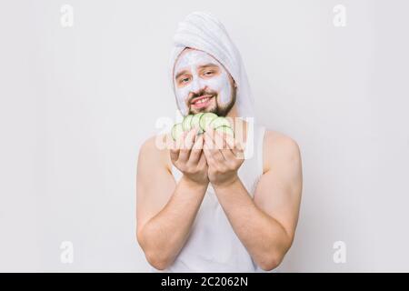 Bellezza, cura della pelle per gli uomini e concetto di spa. Ritratto di felice uomo caucasico portatore di cetrioli freschi e sorridente, con maschera facciale sul viso Foto Stock