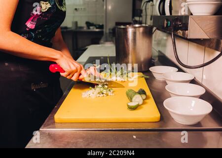 Azienda femmina rosso e coltello per il taglio di cipolla fresca e verde cetrioli. Foto Stock