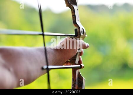 La mano dell'uomo sfocia lo sfondo di tiro con l'arco in primo piano durante un concorso con l'arco. Messa a fuoco selettiva Foto Stock