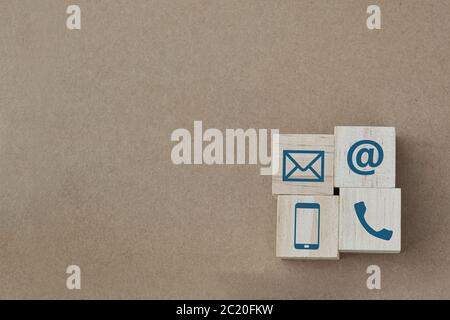 Cubo di legno con icone di Telefono, e-mail e posta su sfondo di carta marrone. Spazio di copia. Contattaci. Foto Stock