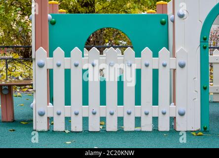 Pannelli recintati in legno bianco sul parco giochi per bambini. Parco giochi con recinzione e parete blu con finestra rotonda Foto Stock