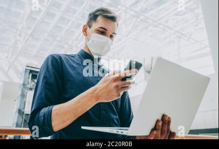 il giovane uomo in una maschera protettiva sta scegliendo un contatto nel suo smartphone Foto Stock