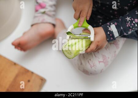 Vista closeup della bambina che peeling cetriolo con un pelatore. Foto Stock