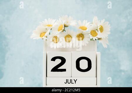 Calendario cubo bianco per luglio decorato con fiori margherita su blu con spazio copia Foto Stock