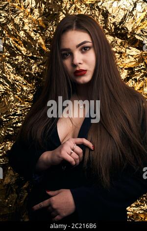 Elegante ragazza chubby che si posa in una giacca nera su uno sfondo dorato. Foto Stock