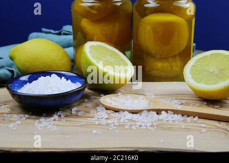 Preparazione di limoni salini sott'aceto conservati marocchini: Primo piano di agrumi gialli isolati a fette, ciotola blu e cucchiaio di legno con sa mare grosso Foto Stock