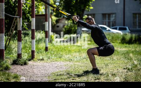 Giovani attractiveman non formazione di sospensione con cinghie di fitness all'aperto nella natura. Foto Stock