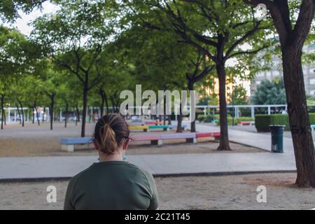 Donna in una maschera seduta in una panchina, maschera protettiva contro il coronavirus, su un parco urbano, godendo della natura durante un focolaio di coronavirus, covid-19 Foto Stock
