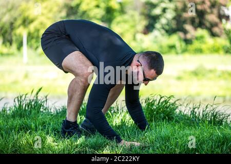 Bello, muscolare, forte uomo di formazione vicino lago facendo yoga. Sportivo adulto concentrato facendo esercizi di spinta in su. Foto Stock