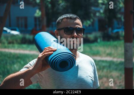Giovane sportivo con un tappeto blu al parco. Giovane uomo che pratica yoga fitness esercizio all'aperto. Foto Stock