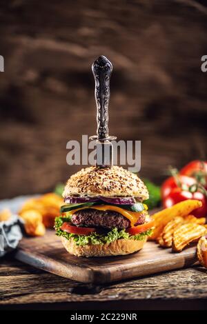 Coltello pugnalato in un hamburger con zeppe di patate su un lato in un ambiente rustico scuro Foto Stock