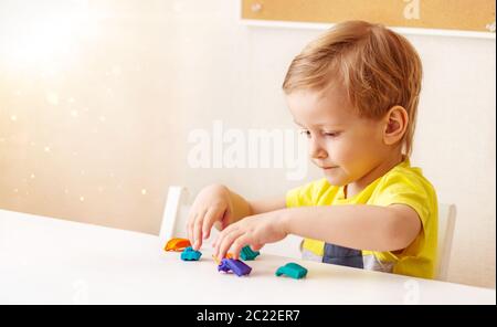 Caucasica baby bionda scolpisce da pasta per bambini per scolpire a casa al tavolo, bambini e creatività, lo sviluppo di belle capacità motorie Foto Stock