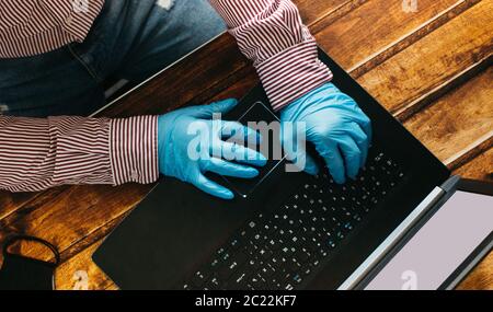 Un uomo che lavora da casa su un computer portatile indossando guanti monouso per la protezione. Focolaio di coronavirus. Uomo d'affari in quarantena. Lavoro a casa. Soggiorna in Foto Stock