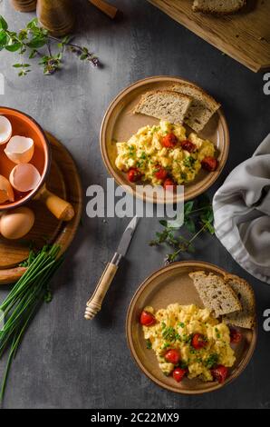 Uova strapazzate con erbe aromatiche, pomodori arrosto, erba cipollina Foto Stock