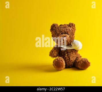 Brown orsacchiotto con una zampa bendato seduto su uno sfondo giallo Foto Stock