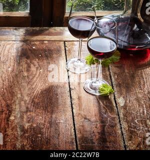 Due bicchieri di vino rosso con un decanter o caraffa su una tavola in legno rustico a fianco di una finestra in un quadrato con un angolo elevato close up con spazio di copia Foto Stock