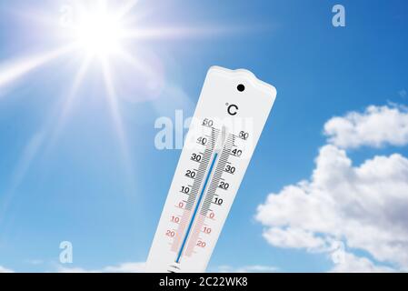 termometro per esterni che indica temperature elevate contro il cielo e il sole blu estivo Foto Stock