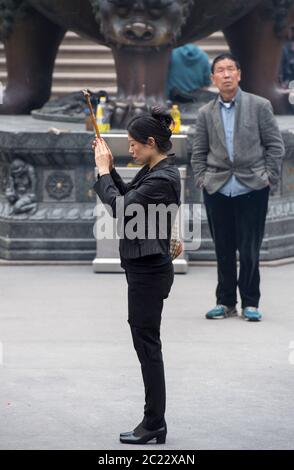 Donna che tiene un bastone di incenso al Tempio di Jing'an a Shanghai, Cina Foto Stock