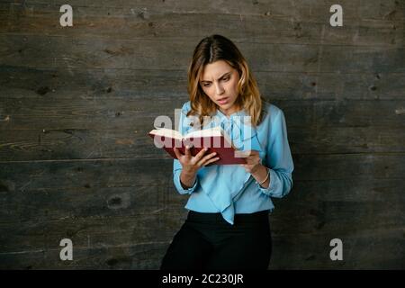 Considerato attraente business donna la lettura di un libro, sembra molto pensieroso. Vestito in Elegante camicetta classica. Foto Stock