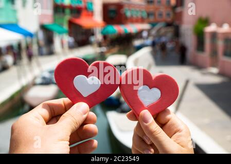 Close-up di un paio di mani che tengono il cuore rosso forma contro Case sfocata a Venezia Foto Stock