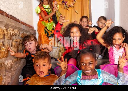 Grande gruppo vario di capretti osservanti spooky in costumi di Halloween che si levano in piedi davanti alla porta della casa Foto Stock