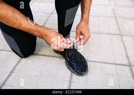 Vista ravvicinata del maschio di legatura a mano i suoi lacci delle scarpe durante l'allenamento all'aperto. Sport concept. Foto Stock